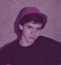 a young man wearing a hat in front of a pink wall